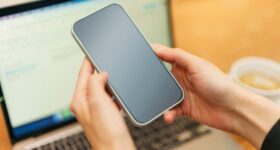 Händer håller en smartphone framför en bärbar dator