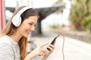 Teen girl listening to the music with headphones in a train station while she is waiting